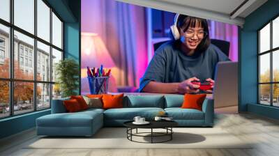 Young asian woman enjoy playing video game by talking on headphones in living room at night. Wall mural