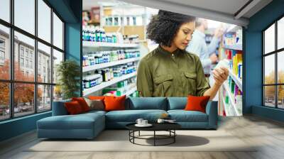 Pharmacy, health shop and woman with medicine for reading label, check product and choice in retail store. African female person looking at drugstore pills for ingredients, information and shopping Wall mural