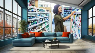 Pharmacy, shopping and woman search for medicine and product in a retail store. Pharmaceutical, drugs and pills with a African female person looking at box for ingredients and information in shop Wall mural