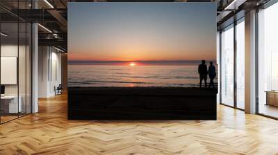 Two people, man and woman, watch the sunrise at the ocean Wall mural