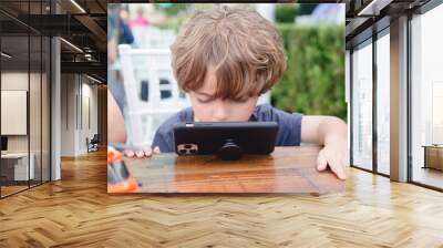 boy with phone in a resturant eating and watching a movie while parents are eating  Wall mural