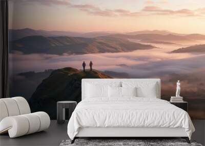 Two hikers standing on a mountain peak during a beautiful sunrise with misty valleys below Wall mural