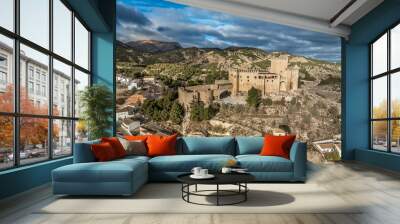 Aerial view of  Velez Blanco castle on a hilltop and town with one or two floor houses whitewashed walls and tiled roofs with dramatic cloudy sky in Andalusia Spain Wall mural