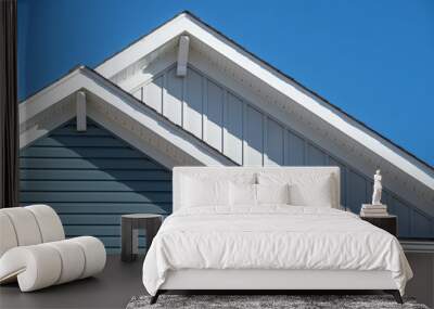 Double gable, with white decorative corbel, bracket, brace on a triangle gable roof, white soffit and fascia,  gray vertical and blue horizontal vinyl lap siding with blue sky background Wall mural