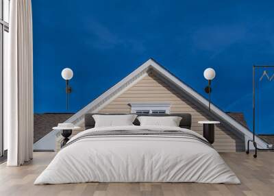 Single gable close up with beige vinyl siding on luxury single family residential home with double attic window in white frame with blue sky background Wall mural