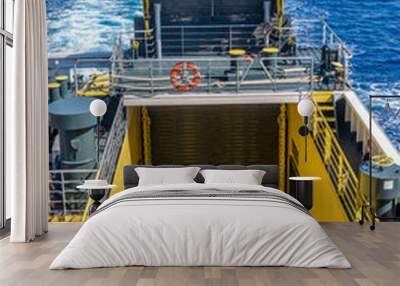 Yellow ramp and draw bridge on a ferry carrying trucks, buses and cars between two Greek islands Wall mural