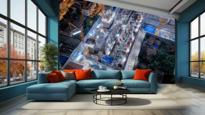 Aerial view of busy industrial construction site workers with cranes working. Top view of development high rise architecture building at night. Wall mural