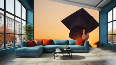 A graduate throws their cap in the air at sunset. Wall mural