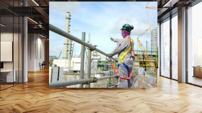 Foreman, supervisor, engineer standing on scaffolding and put on safety harness during working at Height to controls work for support building construction site of petrochemical plant, oil and gas. Wall mural