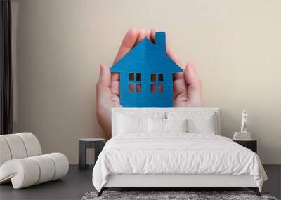 A blue house in the hands on a beige background, a real estate concept for a home and apartment. Below is a view of a female pair holding a blue paper cutout model shape with windows Wall mural