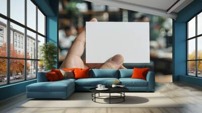 Hand displaying a blank business card with a busy office environment in the background Wall mural