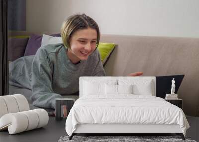 Happy teenage girl blogger working online on laptop with smartphone on sofa at home. Concept of distance education or learning, online shopping, communication with friends Wall mural