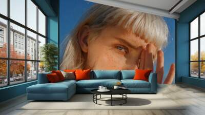 ?lose-up portrait of young blonde with blue eyes with freckles. Portrait of beautiful girl with natural makeup against blue sky Wall mural