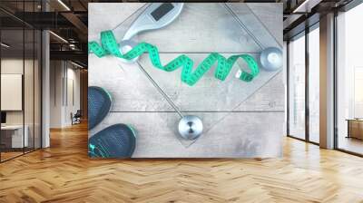 green measure tape, glass weighing scale, running shoes on a rustic surface. weight management and h Wall mural