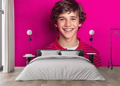 A happy teen boy wearing a pink and red striped polo shirt smiles brightly against a bold magenta background, radiating youthful energy Wall mural