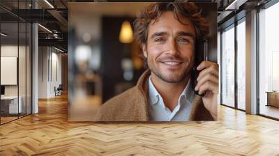 A smiling man in casual clothing holds a phone to his ear, with soft lighting and warm tones highlighting his relaxed and confident demeanor Wall mural