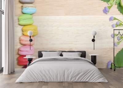 vertical line of colorful fresh sweet cake macarons on left size and little purple flower with green leaves on right size on the wood table background , have copy space for put text. Wall mural