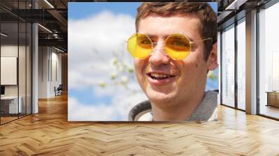 Portrait of handsome man wearing yellow sunglasses on spring background. Funny man outside. 20s male. Portrait face. Out of focus Wall mural