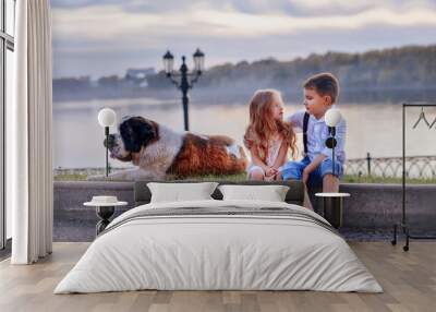 Friends. Tenderness. Love. Children smile and hold hands. The boy looks at a beautiful girl with blond long hair. Brother and sister. Children walk by the water with a Saint Bernard dog. Flashlight. Wall mural