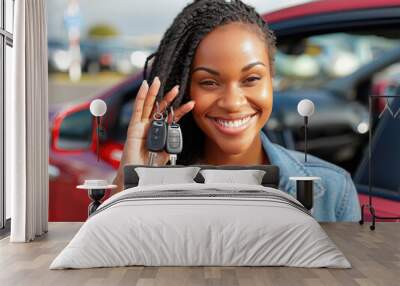 Joyful African American woman posing with car keys and smiling near a red car Wall mural