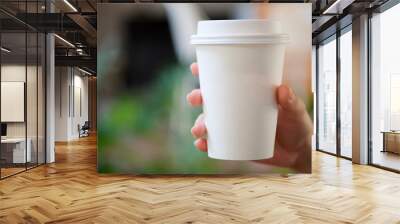 Woman hand holding white paper cup of hot coffee in cafe. Wall mural