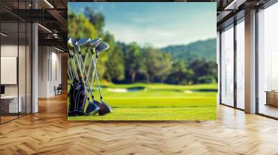 Golf clubs are neatly arranged beside a golf bag on a vibrant fairway, surrounded by trees and rolling hills, showcasing a peaceful afternoon at the course. Wall mural