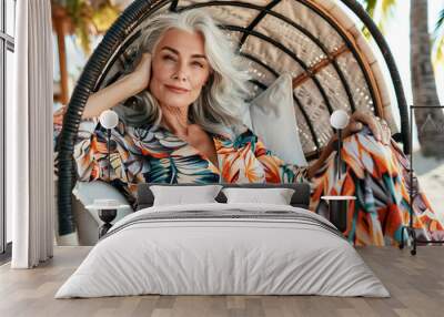 Beautiful senior woman with long grey hair in elegant dress sitting on a beach chair on a tropical resort. Wall mural