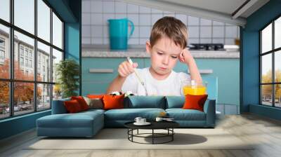 sad little boy sits at the dining table and looking in the plate Wall mural