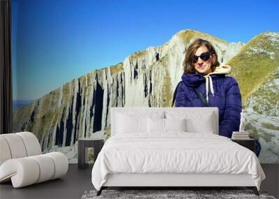 A smiling girl in sunglasses sits in a lotus position on top of a mountain. Rest on Mount Prutas, Durmitor National Park, Montenegro. Wall mural