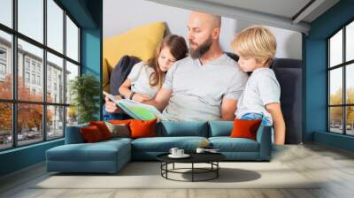  dad with son and daughter sitting on the sofa at home and reading the book together Wall mural