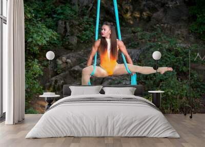 Beautiful aerialist girl doing acrobatic and flexible tricks on blue aerial silks tissues outdoors. Day light. Wall mural