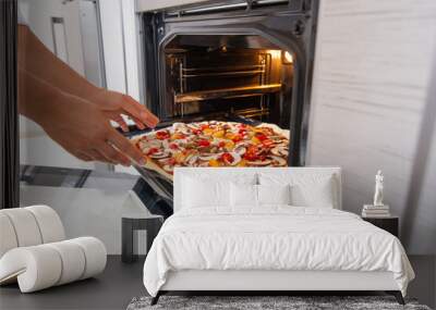 A young woman cook puts a blank vegan pizza in the oven. Wall mural