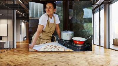 Attractive young woman, housewife wearing chef's apron cooking dumplings. Ukrainian national dish homemade varenyky Wall mural