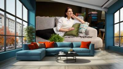 Beautiful European woman lying on a stylish modern sofa, inspecting and testing it for durability and comfort before buying it in the upholstered furniture shopping mall Wall mural