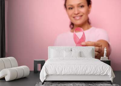 Blurred smiling African woman in pink t-shirt holding satin ribbon in her hand. Breast and abdominal cancer awareness, October Pink day on colored background, copy space. Breast cancer support concept Wall mural