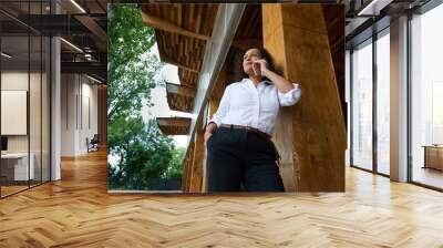 Confident businesswoman talking on smartphone under wooden architecture Wall mural