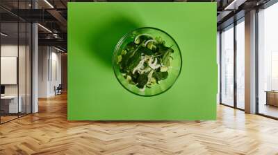 Flat lay of green salad with herbs in transparent glass bowl on green background Wall mural