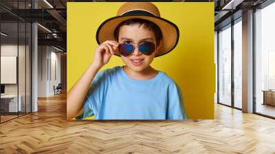 Portrait of a beautiful child boy wearing summer hat and sunglasses, cute posing over yellow background with copy space. Summer holiday concept Wall mural