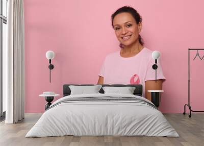 Portrait of an altruist, smiling mixed race woman in a pink T-shirt with a pink satin ribbon, symbol of International Breast Cancer Day. Educational program for the fight against cancer. 1 st October Wall mural