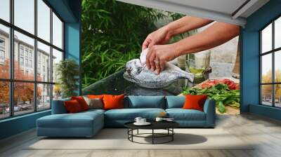 Preparing fresh fish for barbecue with herbs and vegetables outdoors in a garden setting. Culinary process of seasoning, grilling, and enjoying a healthy seafood meal outside. Wall mural