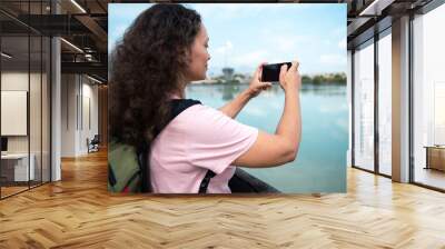 Woman capturing scenic lake view with smartphone outdoors Wall mural