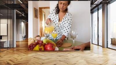 Woman pouring fresh orange juice into glasses for breakfast with family at home, healthy morning routine Wall mural