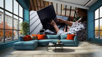 Woman working remotely on a laptop with coffee and smartphone on patio table Wall mural