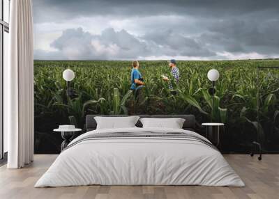 Two farmers in an agricultural corn field on a cloudy day. Agronomist in the field against the background of rainy clouds Wall mural