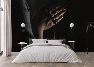 Woman hands holding rosary on black background Wall mural