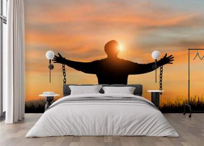 Silhouette of freedom young man standing alone with beautiful sky at sunset open both arms with chains on his arms. He felt free from the shackles tied to his arms. Wall mural