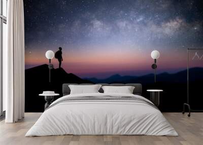 Silhouette of young male traveler with backpack standing and watching the star, milky way over the sky alone on top of the mountain. He enjoyed traveling and was successful when he reached the summit. Wall mural