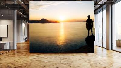 Young man standing on cliff looking beautiful view sunrise over the sea and sky in summer. Wall mural