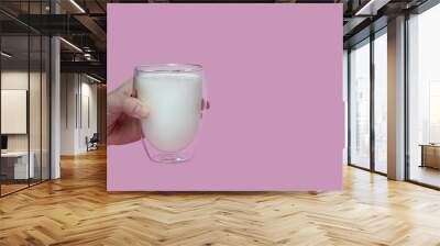 female hand holding a glass with fresh milk, on a pink background,fortified drink, calcium Wall mural