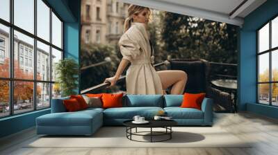 Full height portrait of a stylish blonde woman with long legs in elegant leather trench coat and smoky eyes makeup in the outdoor on the balcony. Spring - autumn fashion concept. Soft selective focus. Wall mural